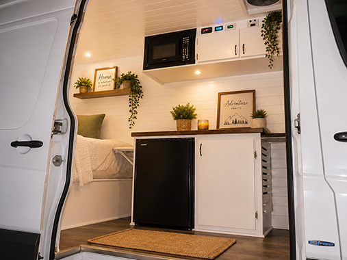 Interior of a finished camper van conversion with cabinetry, butcher block galley, and slatted ceiling